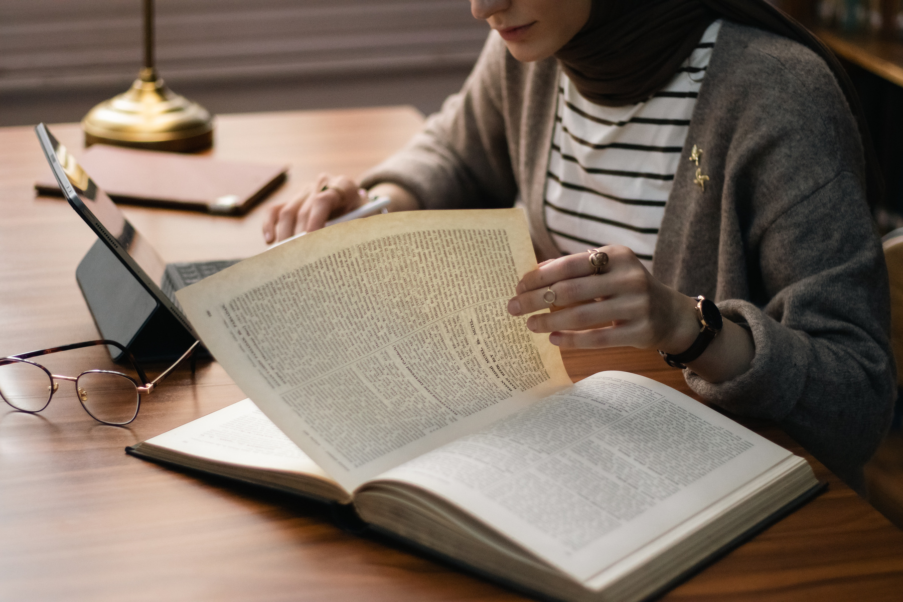 Woman Reading Book with Tablet on Table